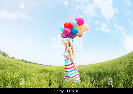 Happy woman with colorful balloons in field on blue sky background Stock Photo