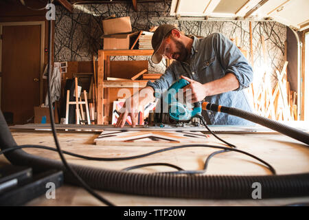 Serious craftsperson using circular saw on wooden plank at workshop Stock Photo