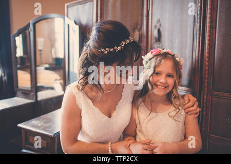 Portrait of happy flower girl with bride standing by cabinet at home Stock Photo