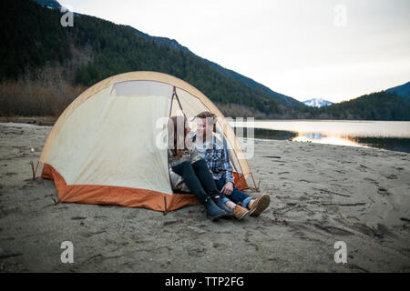 Young couple looking face to face while sitting in tent at lakeshore Stock Photo