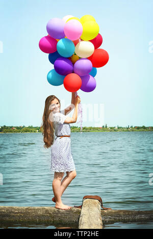 Happy woman with colorful balloons on river coast Stock Photo