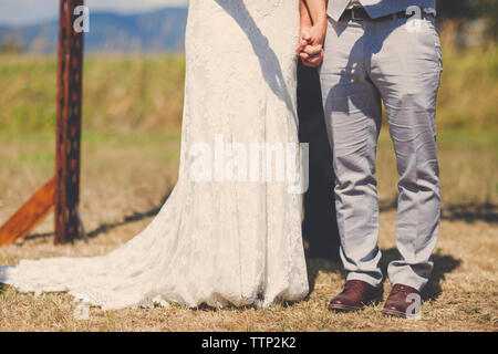 Low section of newlywed young couple holding hands while standing on field Stock Photo
