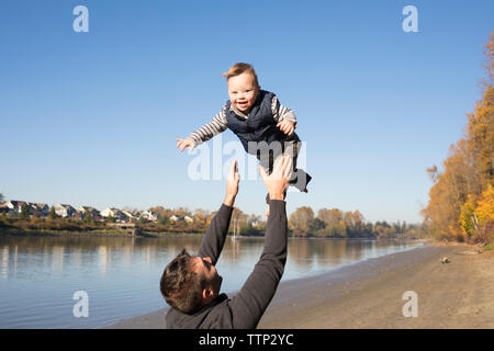 Rear view of happy father throwing daughter while standing at Brae Island Regional Park against clear sky Stock Photo