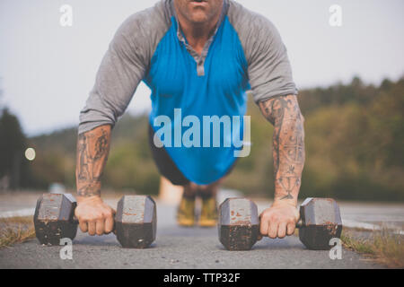 Low section of man with dumbbells doing push-ups on road at park Stock Photo