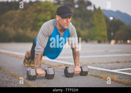 Man with dumbbells doing push-ups on road at park Stock Photo