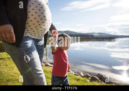 Pregnant mother and son holding hands while walking on lakeshore Stock Photo