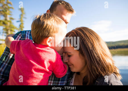 Loving son touching mother's head while being carried by father against lake Stock Photo