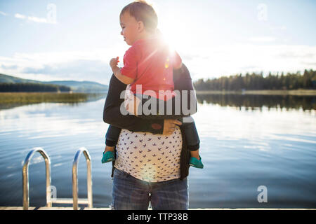 Pregnant mother carrying son by lake during sunny day Stock Photo
