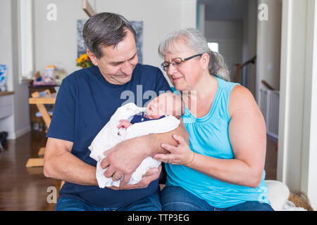 Grandparents with cute newborn granddaughter sitting in living room at home Stock Photo