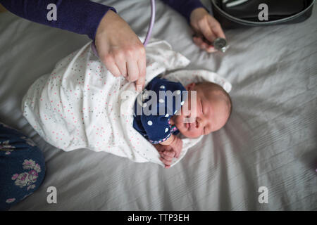 High angle view of midwife examining cute newborn sleeping baby girl with stethoscope on bed at home Stock Photo