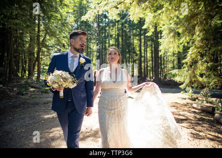Newlywed couple holding hands while walking against trees in forest Stock Photo