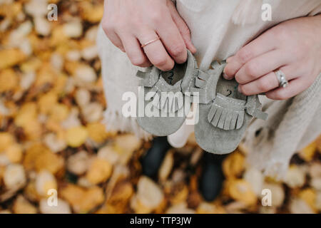 High angle view of pregnant woman holding baby booties while standing in forest during autumn Stock Photo