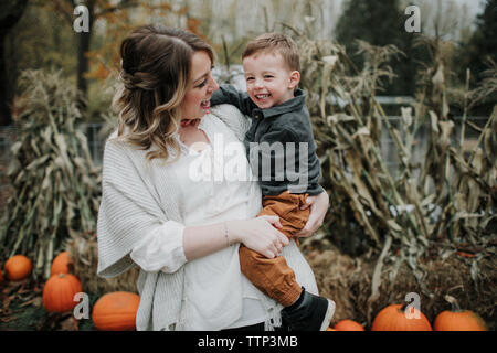 Cheerful mother carrying cute son on pumpkin patch during autumn Stock Photo