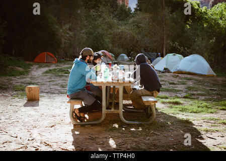 Family having drinks while sitting on picnic table in forest Stock Photo