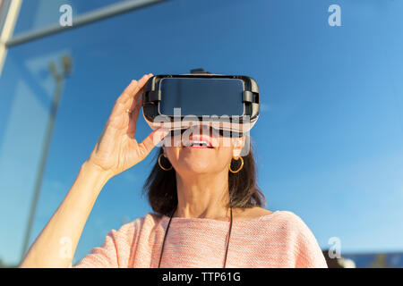 Woman using VR glasses while standing against building Stock Photo