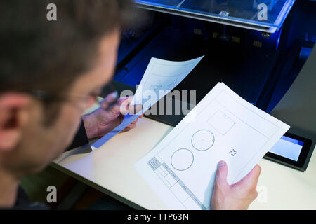 Engineer holding documents by 3D printer at table in office Stock Photo