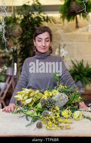 Smiling senior woman standing at flower shop desk with flowers Stock Photo