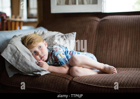Full length of frightened boy lying on sofa at home Stock Photo