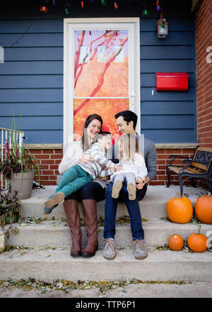 Happy family sitting on steps against house during Halloween Stock Photo