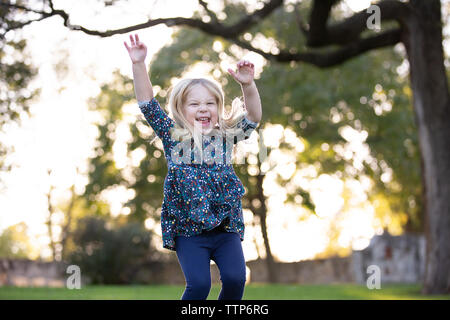 blonde girl jumping with arms in air outside and smiling big Stock Photo