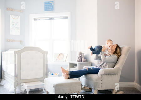 Mom in chair in nursery holding up and kissing baby boy Stock Photo