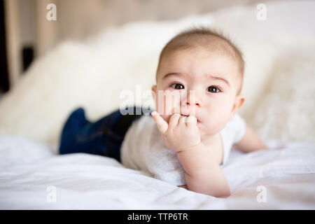 Cute brown eyed baby boy laying on bed with fingers in mouth Stock Photo