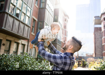 Smiling dad holding smiling baby boy up in air outdoors in city Stock Photo