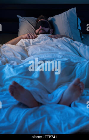Man wearing sleep mask while sleeping on bed at home Stock Photo
