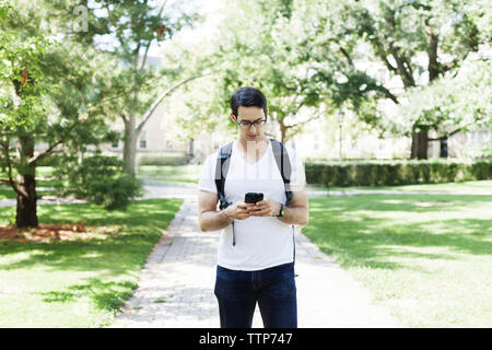 Confident man using mobile phone while standing on footpath at park Stock Photo