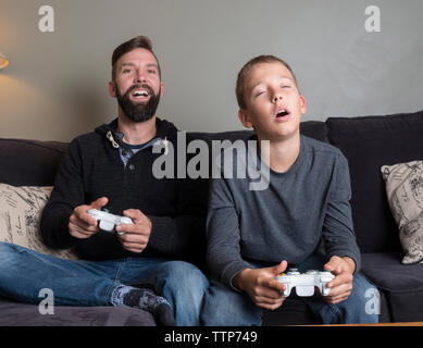Father with son playing video game while sitting on sofa at home Stock Photo