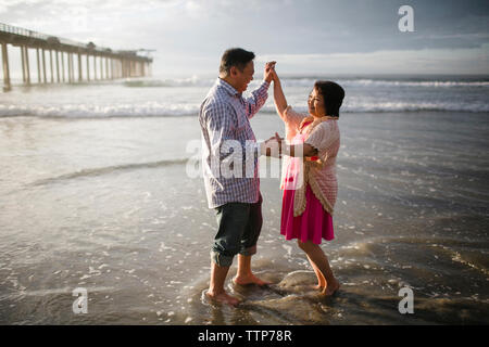 Side view of couple dancing on shore at beach Stock Photo