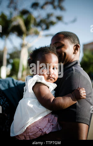 Father carrying crying daughter while standing against sky Stock Photo