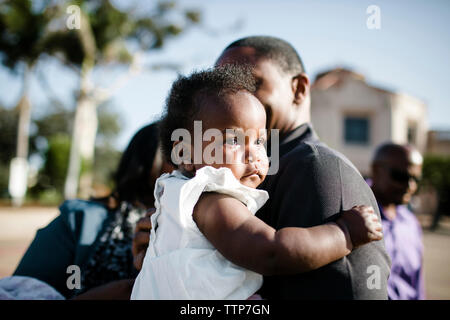 Close-up of father carrying crying daughter while standing against sky Stock Photo