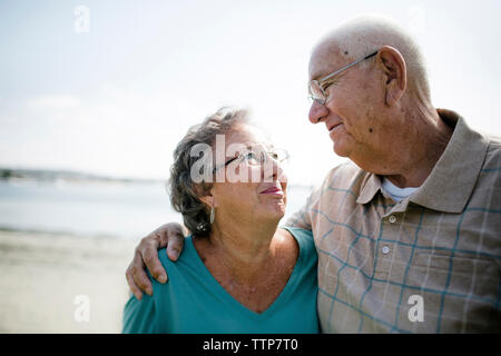 Happy senior couple looking each other face to face while standing at beach against sky Stock Photo