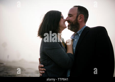 Side view of romantic couple embracing while standing at beach during foggy weather Stock Photo