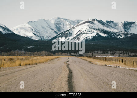 Dirt road leading towards snowcapped mountains Stock Photo