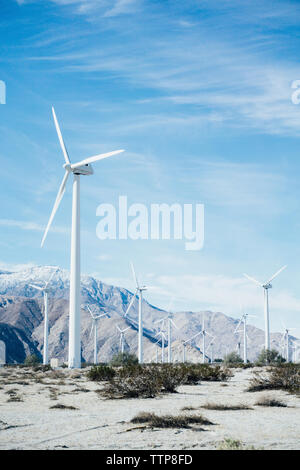 Wind turbines on farm by rocky mountain against sky Stock Photo