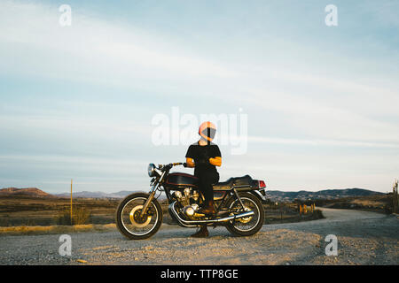 Low angle view of man wearing gloves while riding motorcycle at street against sky Stock Photo