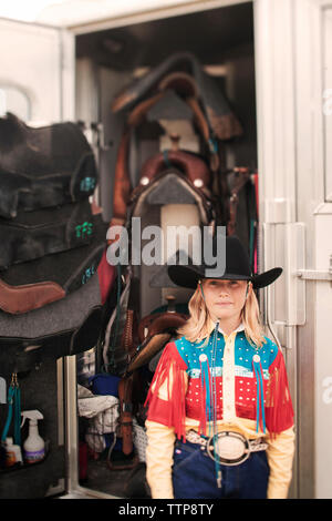 Portrait of girl standing against saddles hanging in stable Stock Photo
