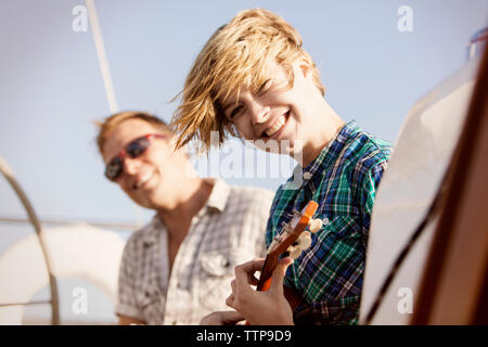 Happy woman holding guitar while travelling with friend on boat Stock Photo