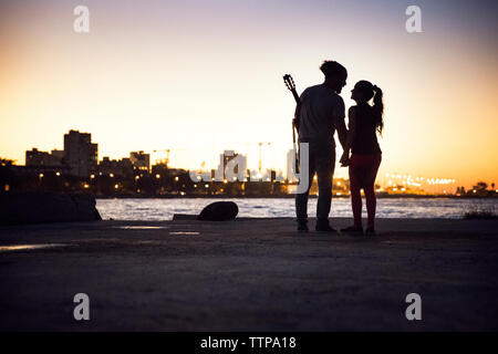 Silhouette couple standing at lakeshore against clear sky during sunset Stock Photo