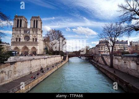 Notre Dame de Paris by river against cloudy sky Stock Photo