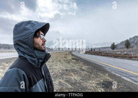 Side view of man wearing hooded jacket while standing on field against Mammoth Mountain Stock Photo