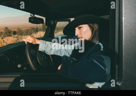 Close-up of thoughtful young woman sitting on driver's seat in off-road vehicle at desert during sunny day Stock Photo