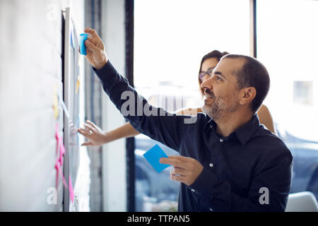 Creative businessman sticking adhesive notes on whiteboard in office Stock Photo