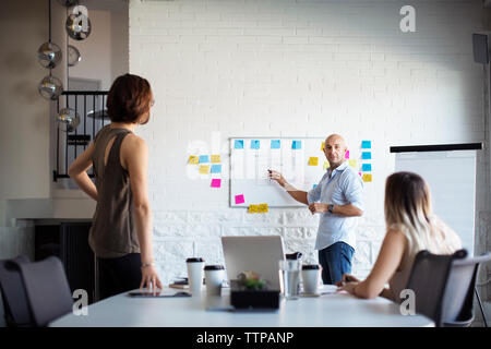 businessman discussing with female colleagues over whiteboard during meeting Stock Photo