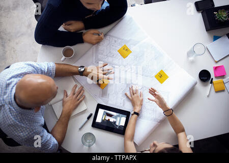 Overhead view of architects discussing over blueprints and digital tablet at creative office Stock Photo