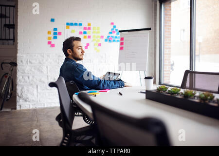 Thoughtful businessman using tablet while sitting on chair in office Stock Photo