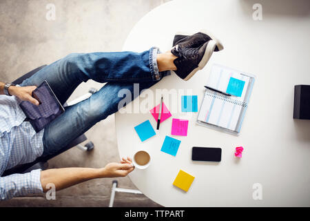 Low section of businessman holding coffee cup and tablet while sitting at creative office Stock Photo