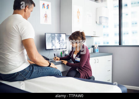 Female doctor writing in book while patient sitting on bed in clinic Stock Photo